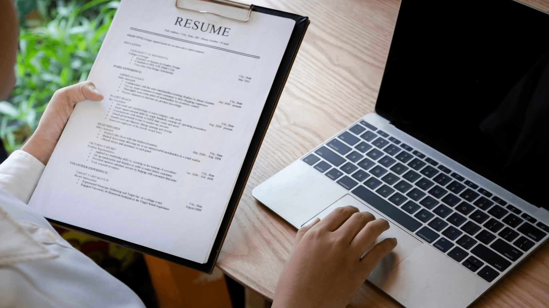 Person holding a resume in front of a laptop